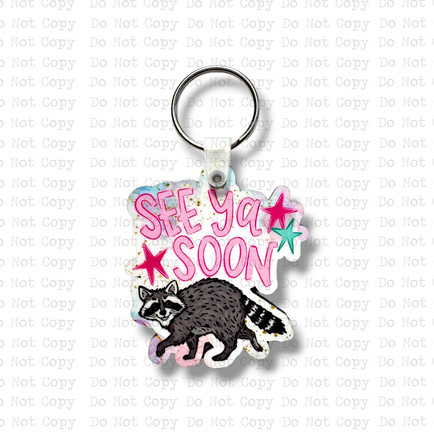 Custom-shaped contoured MDF wood sublimation keychain blank kit featuring a cute cartoon raccoon and text that says See Ya Soon with pink and teal stars, shown with keyring hardware.